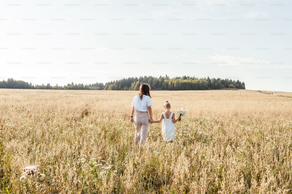 Beautiful young mother and her daughter in field. White clothes, freedom concept. Copy space, rear view.