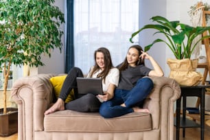 Deux jeunes femmes regardent des séries télévisées sur un ordinateur portable. Plantes vertes, design durable à l’intérieur.