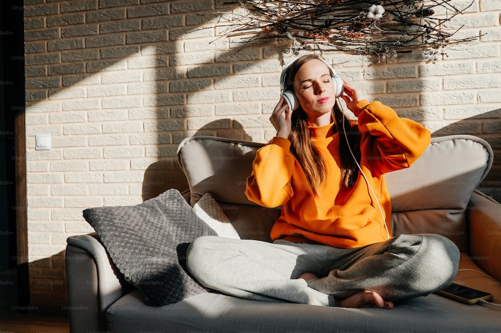 Mujer feliz escuchando música desde el teléfono móvil sentada en un sofá en casa. Día soleado