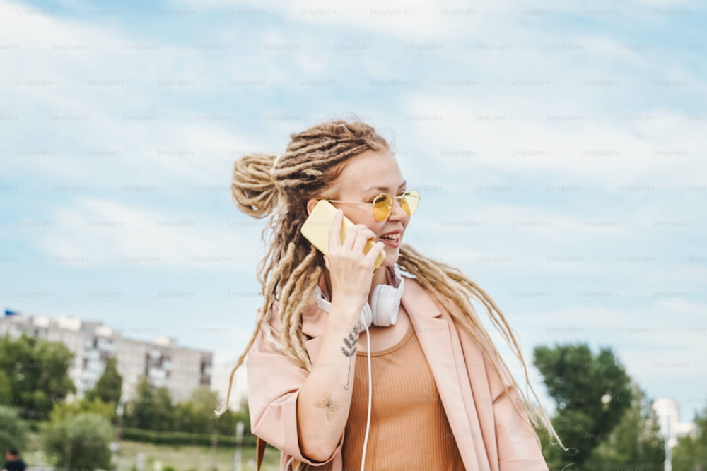 Woman with dreadlocks and sunglasses talking on mobile phone on sky background. Selective focus.