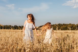 Beautiful young mother and her daughter dance in field. White clothes, freedom concept. Front view.