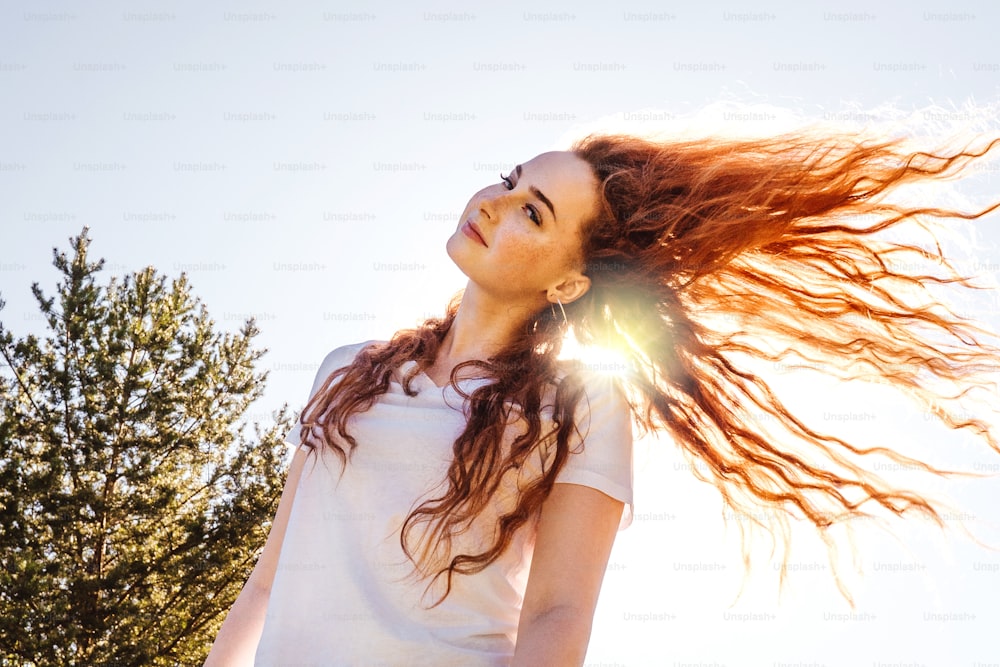 Mulher feliz jovem com longos cabelos encaracolados ao sol. Vida no campo. Camiseta branca.