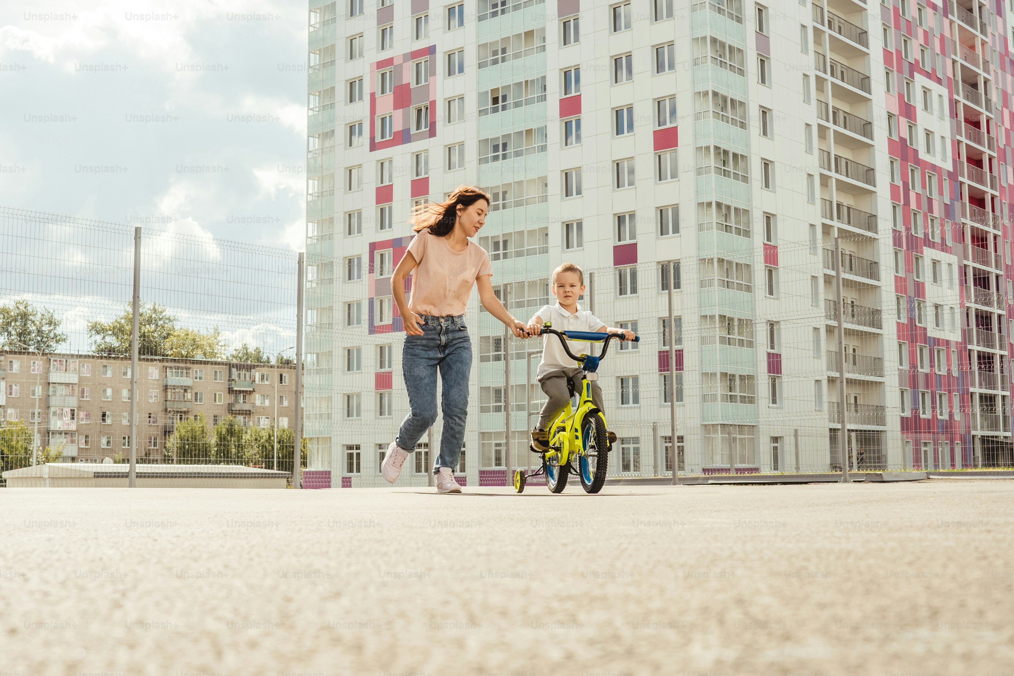 boy rides a bike with his mother. Houses on background, summer.