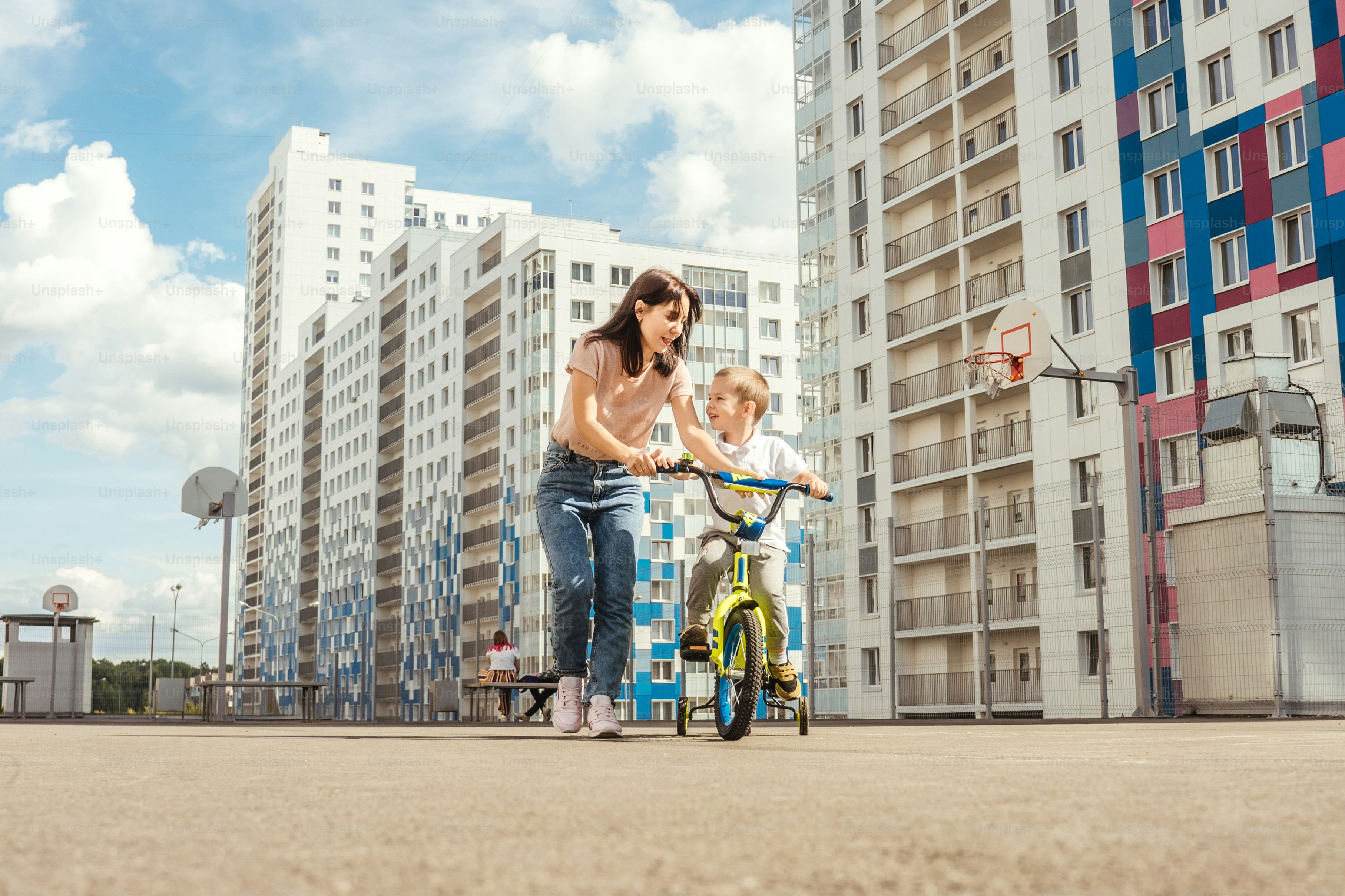 boy rides a bike with his mother. Houses on background, summer.