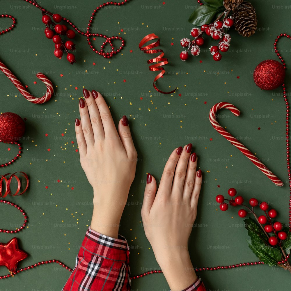 Manucure de Noël. Ongles rouges, mains en chemise à carreaux sur fond vert avec boules de Noël rouges comme cadre.