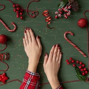 Christmas manicure. Red nails, hands in checkered shirt on green background with red christmas baubles as frame.