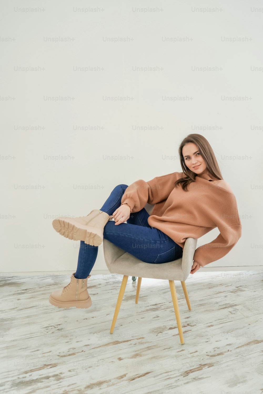 Young attractive woman wearing sweatshirt and jeans on white background studio shot. Woman poses on chair.