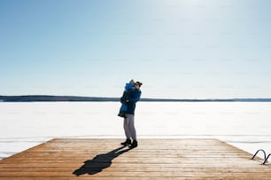 Little boy with father on pier in winter, snow and forest on background. Blue colors.