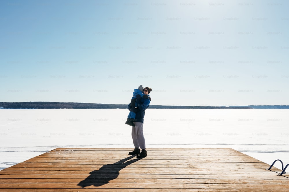 冬の桟橋に父親を持つ小さな男の子、雪と森の背景。青い色。