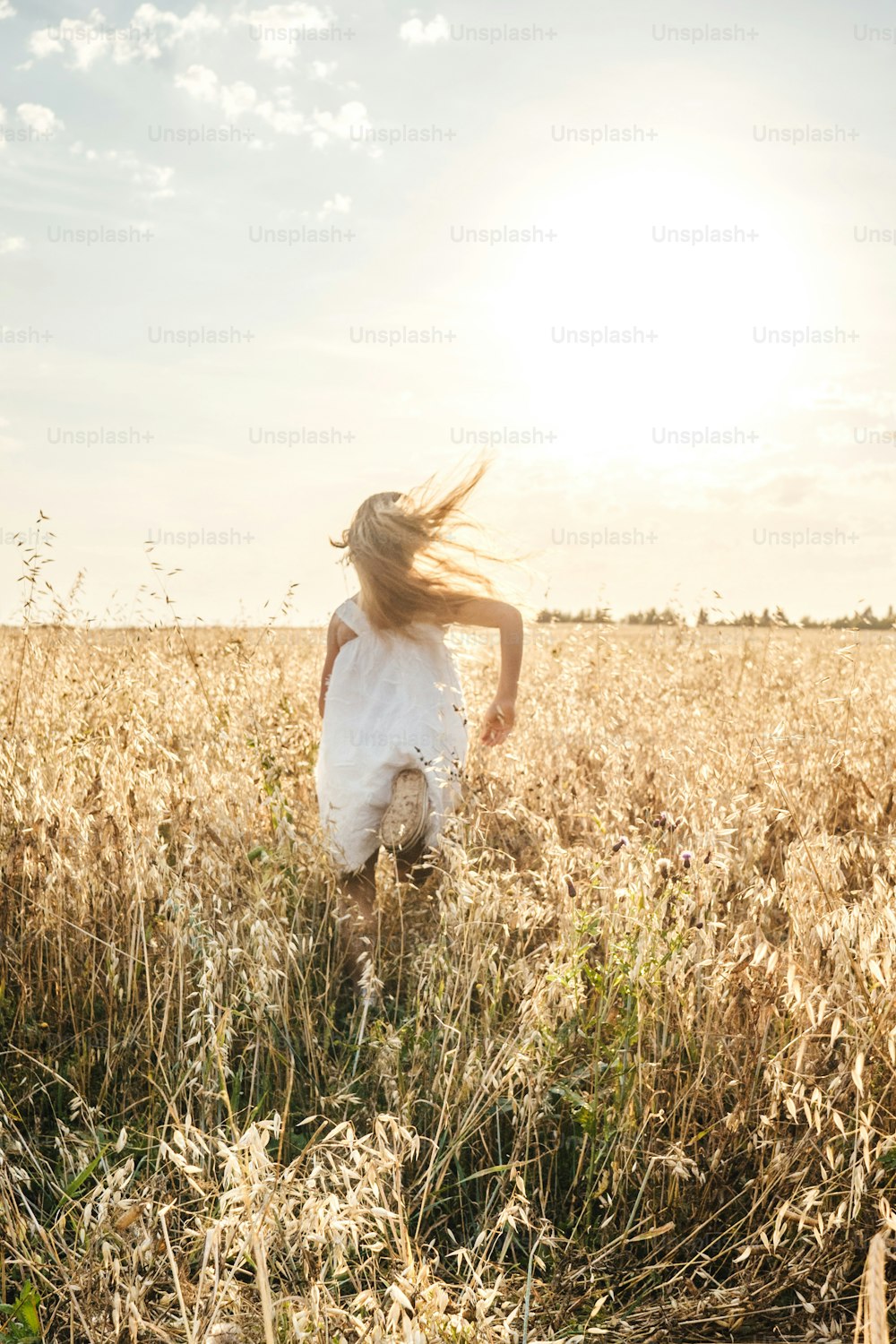 Menina correndo no prado ao longe. Luz do pôr-do-sol, espaço de cópia. Vista traseira.