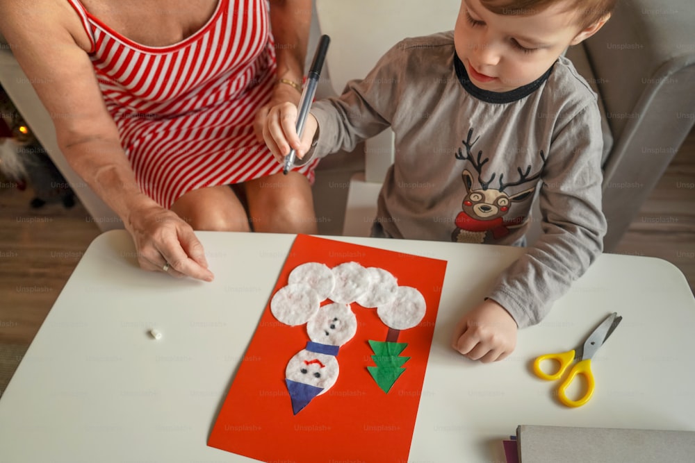 A Little boy with grandmother make Christmas craft, greeting card from cotton pads.