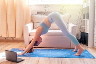 girl doing yoga at home online. Watch tutorial in laptop.