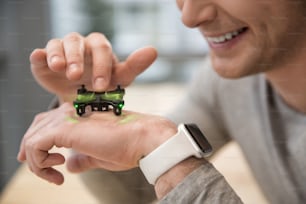 Close up of arm of young man watching at the small quadrocopter in move. He is touching the moving propeller and smiling. There is a smart watch on his wrist
