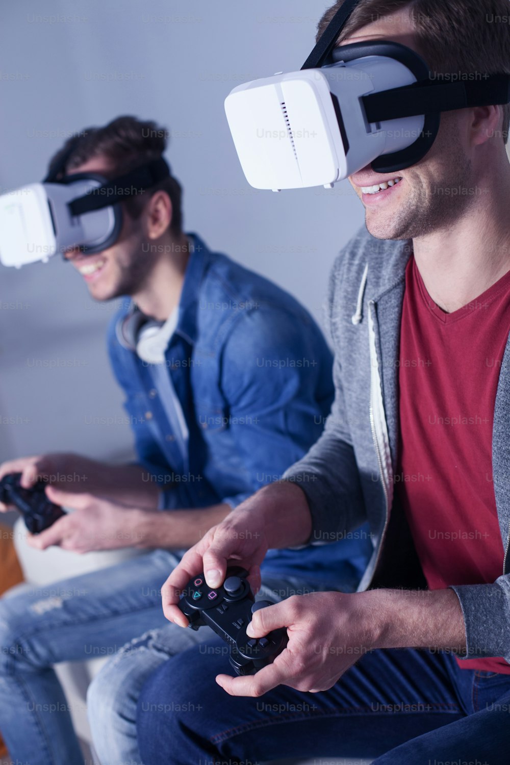 Attractive young men are competing in play station. They are sitting and laughing. The guys are wearing a virtual reality headset