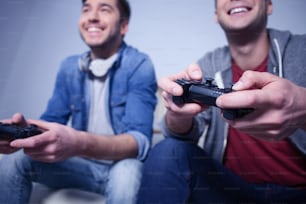 Handsome young men are competing in play station at home. They are sitting and smiling. Focus on their arms holding a game controller