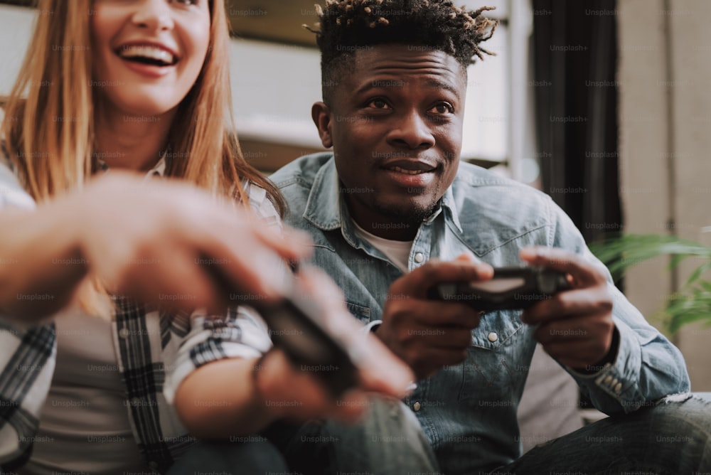Portrait of handsome young man in denim shirt and cropped smiling girl using joysticks. Focus on man