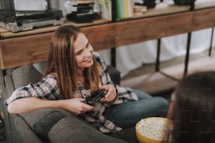 Portrait of charming girl holding game controller while sitting on couch with popcorn