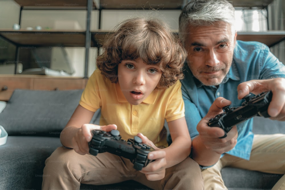 Niño pequeño maravillado sentado cerca de su padre y jugando videojuegos en casa