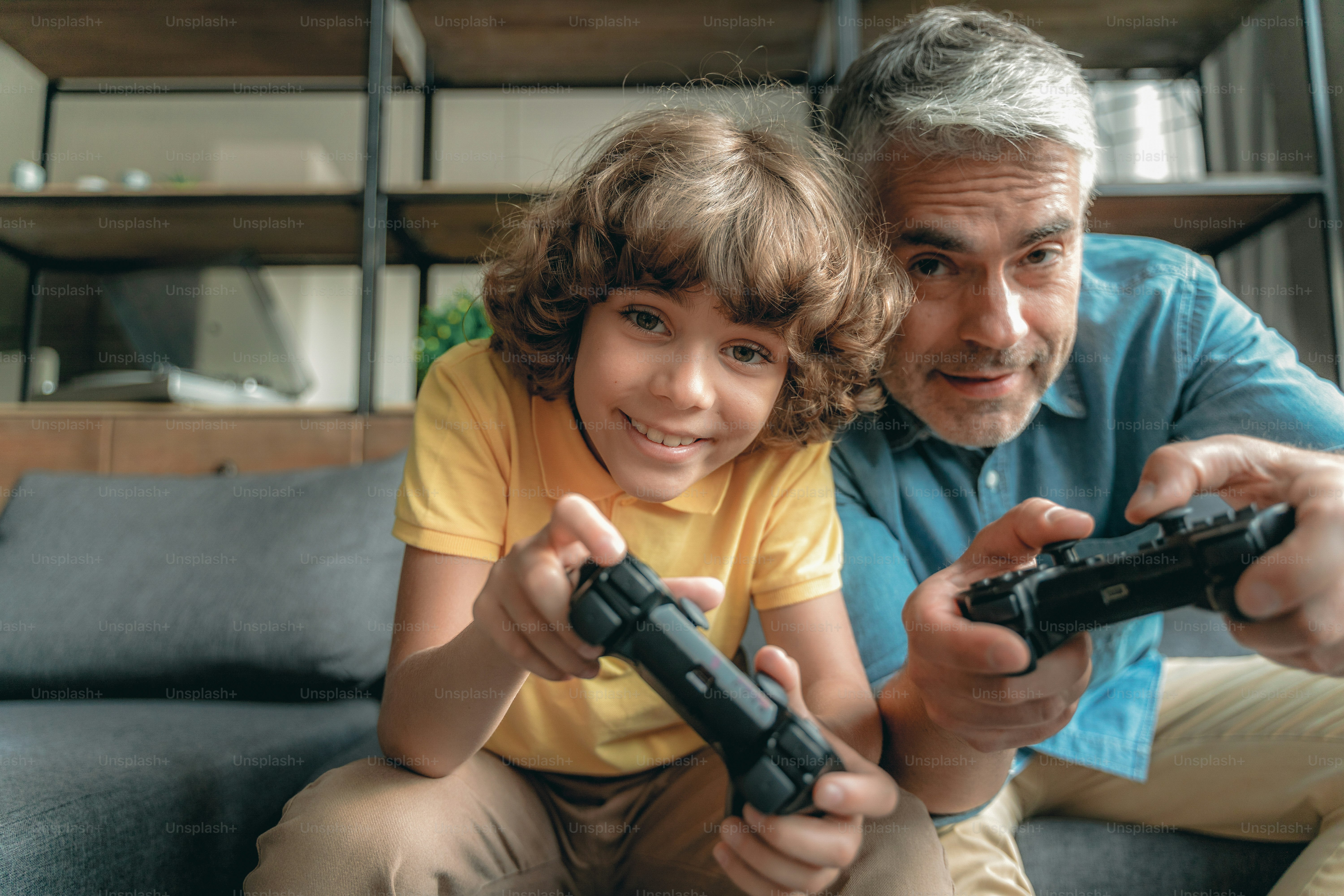 Happy and smiling father sitting sitting near little son and playing in video games
