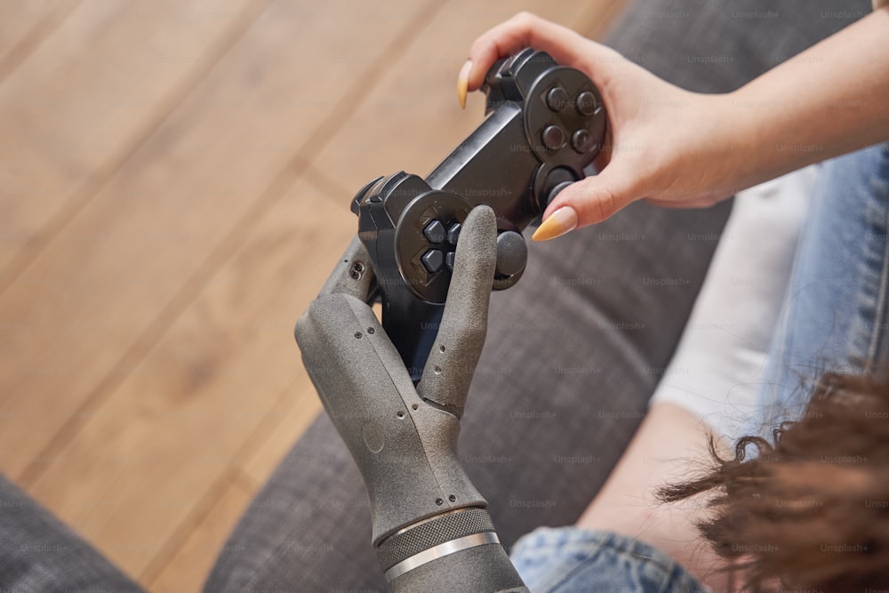 Cropped view of the happy amazed woman with artificial limb playing video game with joystick while spending time at home at the sofa. Stock photo, gaming and technology concept