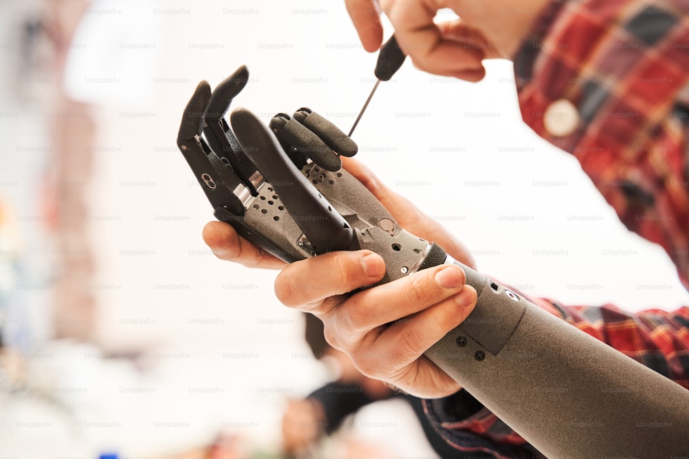 Close up view of the intelligent man scientist twisting with screwdriver contacts in mechanical plastic hand. Man wearing working centrally at his desk in modern laboratory. Stock photo