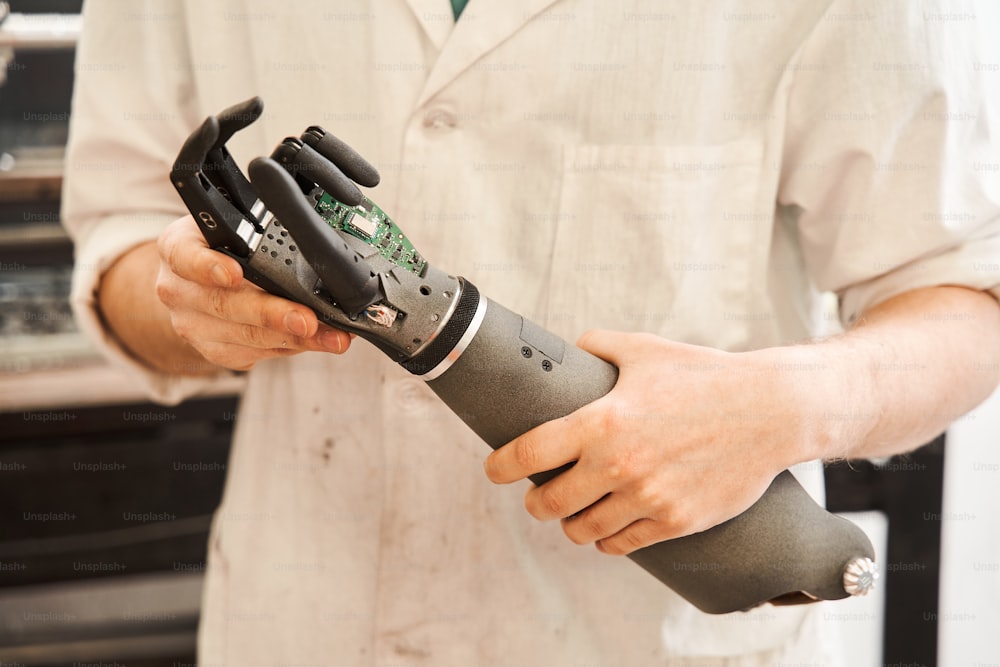 Close up view of the man holding a mechanical arm in his hands while working at the development of bionic prosthesis hand. Engineering of the bionic hands concept. Stock photo