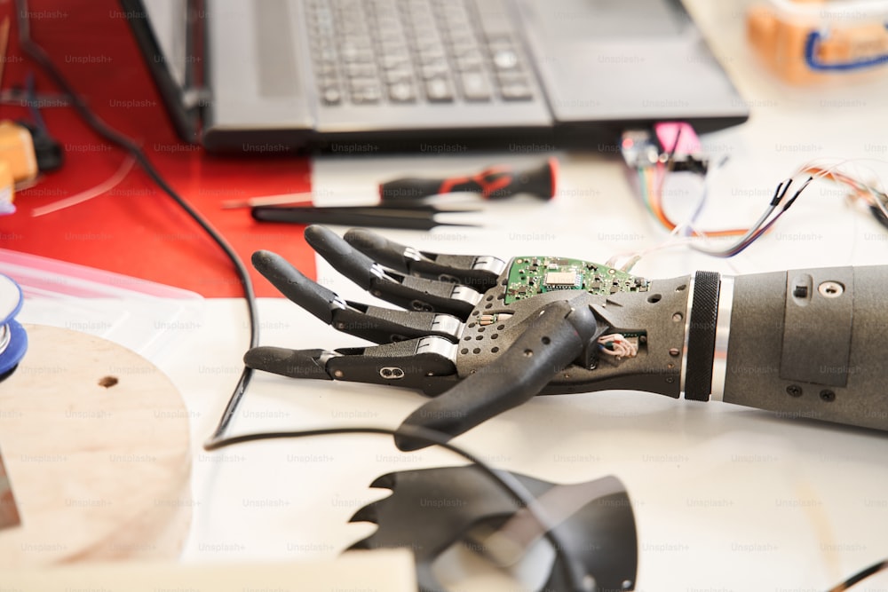 Close up view of the black bionic hand laying at the table while people workers inspecting it during developing at the engineer laboratory. Stock photo