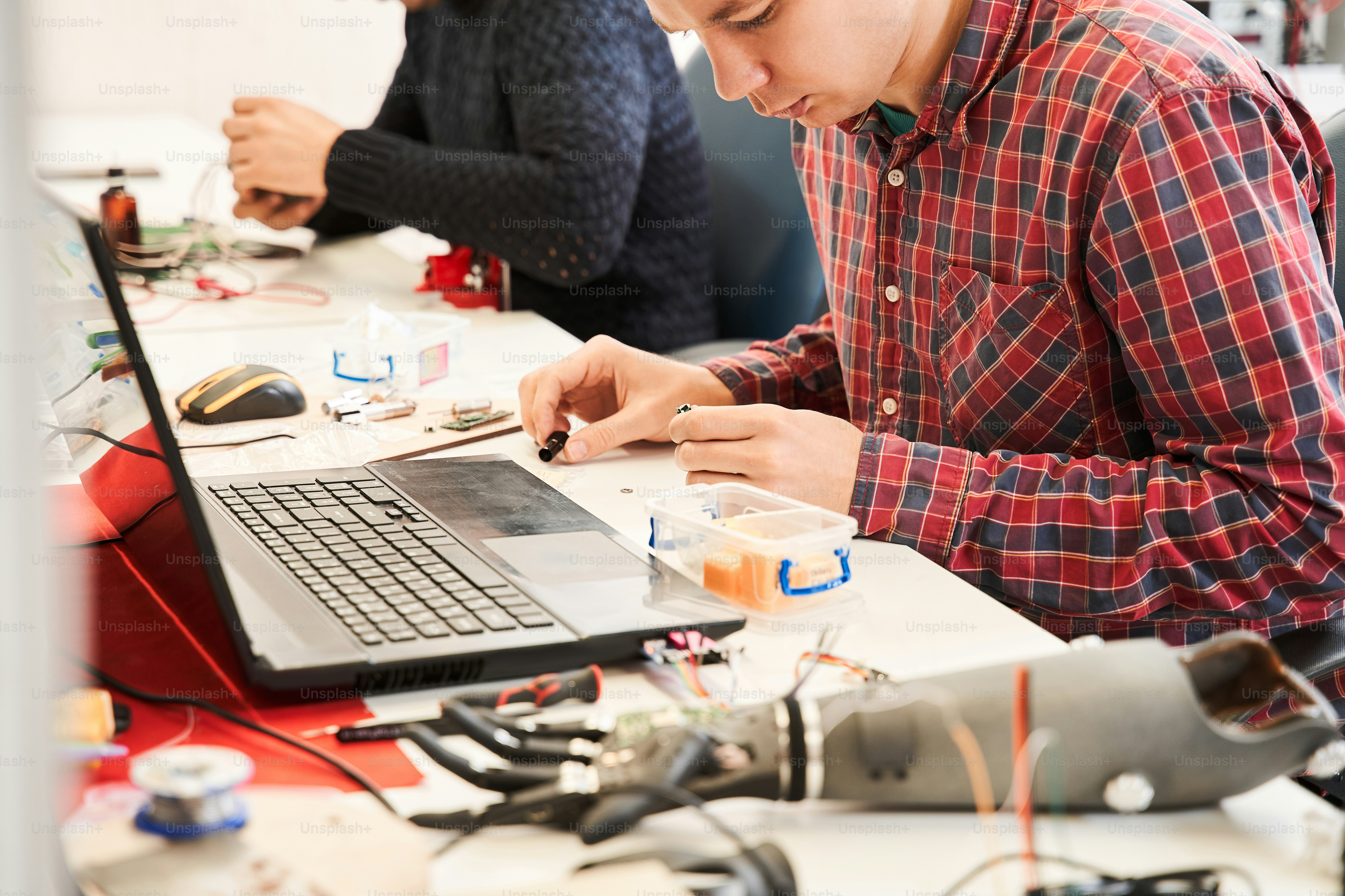People working in laboratory on creating details of mechanism. Workers helping each other to adjust quality of manufacturing elements in order to obtain qualitative invention as result. Stock photo