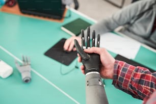 Close up view of young prosthetist holding prosthetic hand and checking it for quality and making adjustments while working in modern laboratory with colleagues