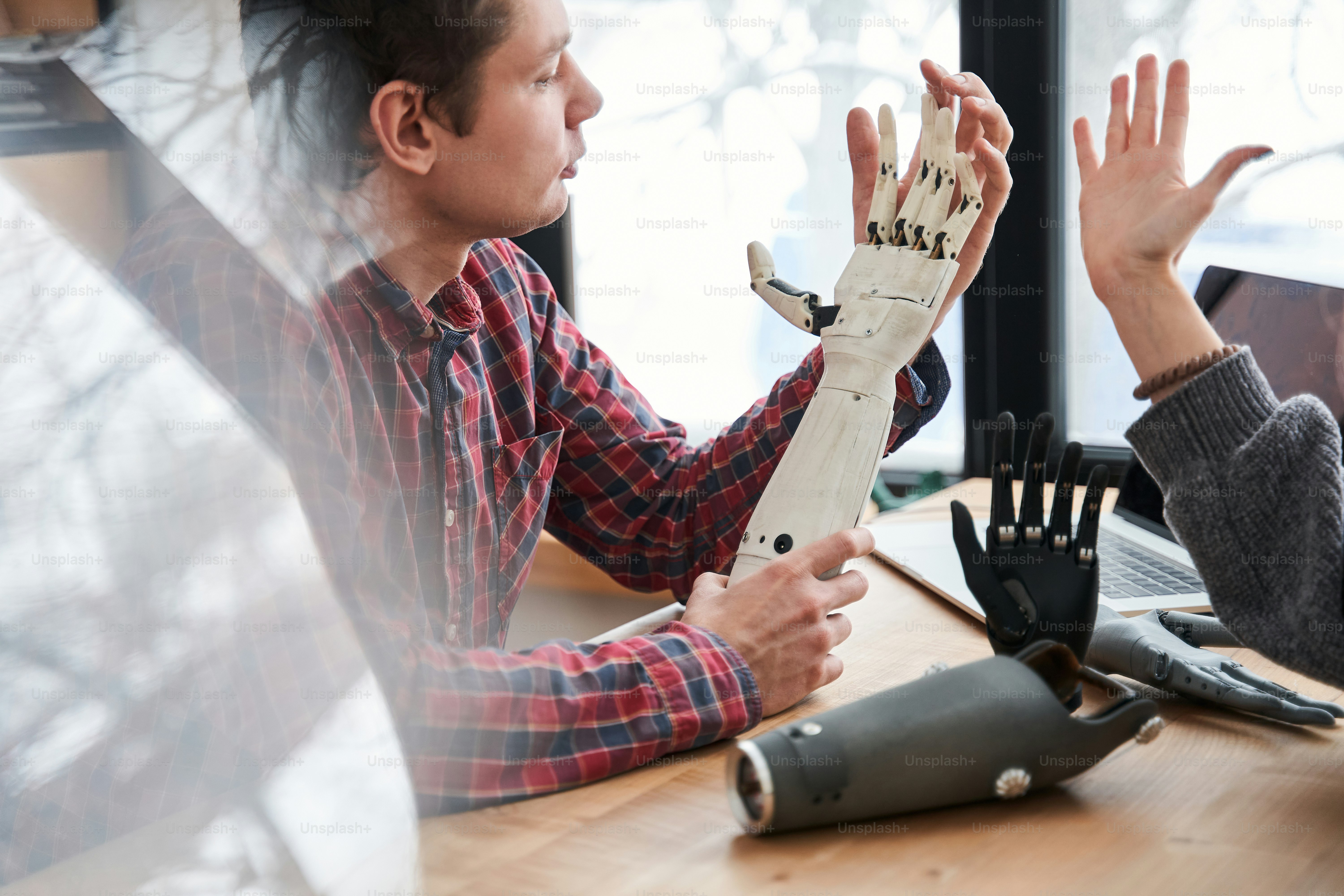私の手と比較してください。同僚とテーブルで作業しながら、義手を注意深く見て実際の手と比較する男性エンジニアの接写。ストックフォト