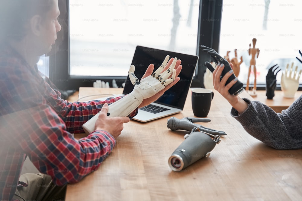 Close up portrait of the male and female colleagues holding bionic prosthesis limbs and discussing it while developing artificial limbs at their workplace. Engineering of the bionic hands concept