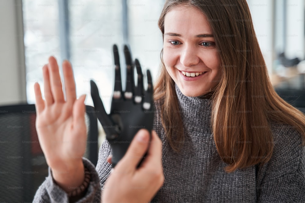 Wow. Close up view of the woman comparing her hand with bionic prosthesis limb while sitting at the engineering office. Engineering of the bionic hands concept. Stock photo