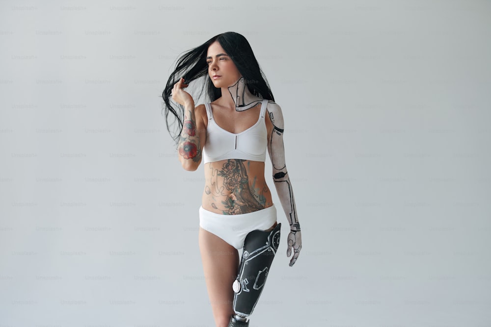인공 다리와 사이버 바디 아트를 가진 문신을 한 여성의 전체 길이 모습이 스튜디오에서 포즈를 취하고 있다. 특이한 외모 개념입니다. 스톡 사진