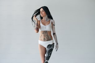 Vista de cuerpo entero de la mujer tatuada con pierna artificial y arte corporal cibernético posando en el estudio. Concepto de apariencia inusual. Foto de archivo