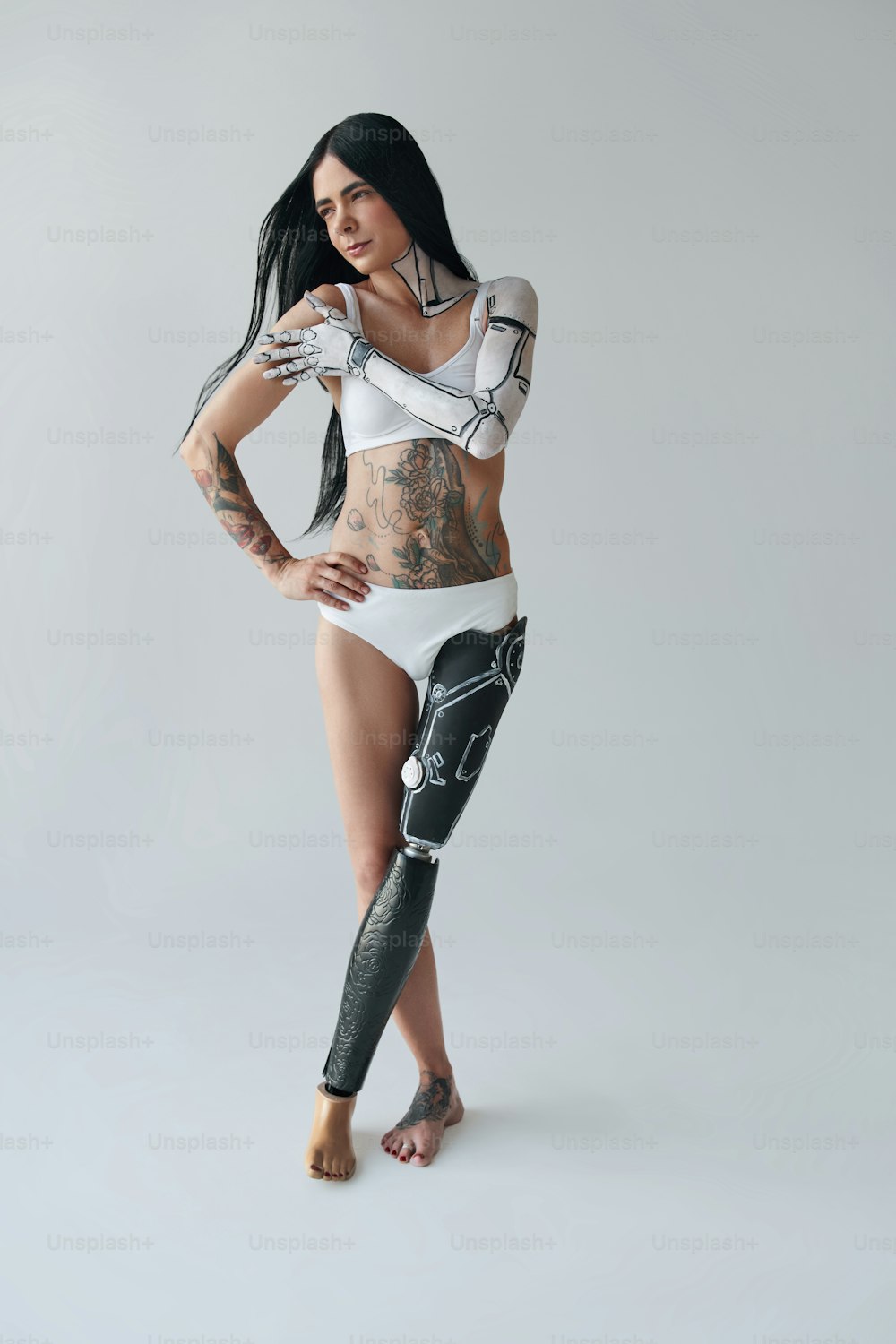 Vista de cuerpo entero de la mujer tatuada con pierna artificial y arte corporal cibernético posando en el estudio. Concepto de apariencia inusual. Foto de archivo
