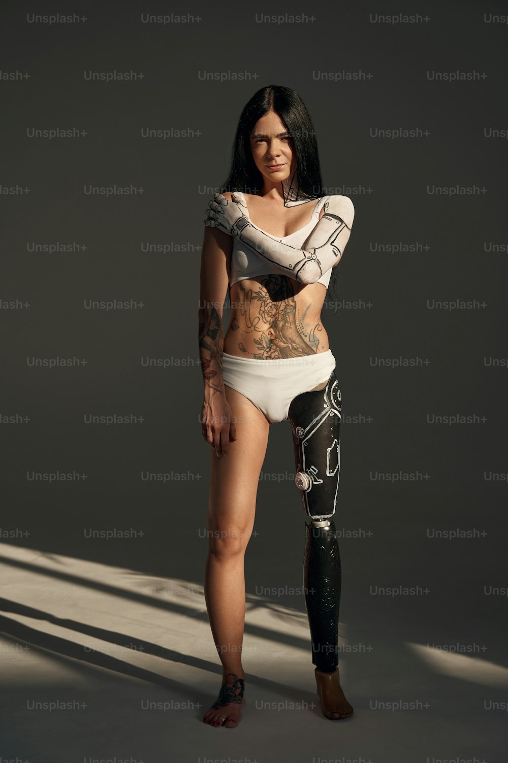 Vista a figura intera della donna tatuata con motivo cyborg sul suo corpo in posa nello studio su sfondo scuro. Persone e concetto di robot
