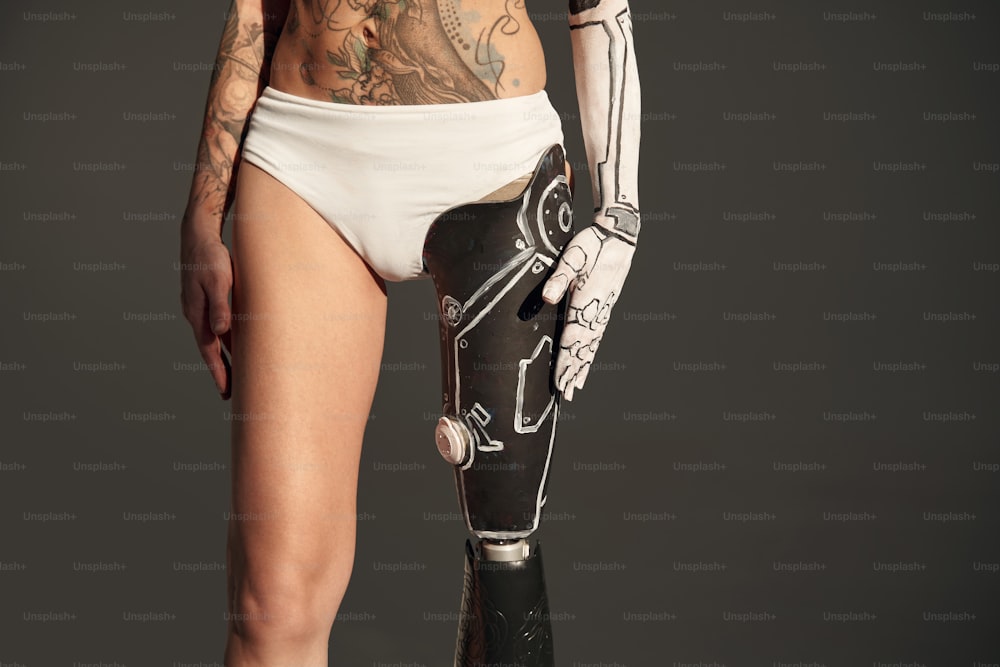 Close up view of the tattooed woman with cyborg body art and with artificial leg standing isolated at the studio. People with special needs concept