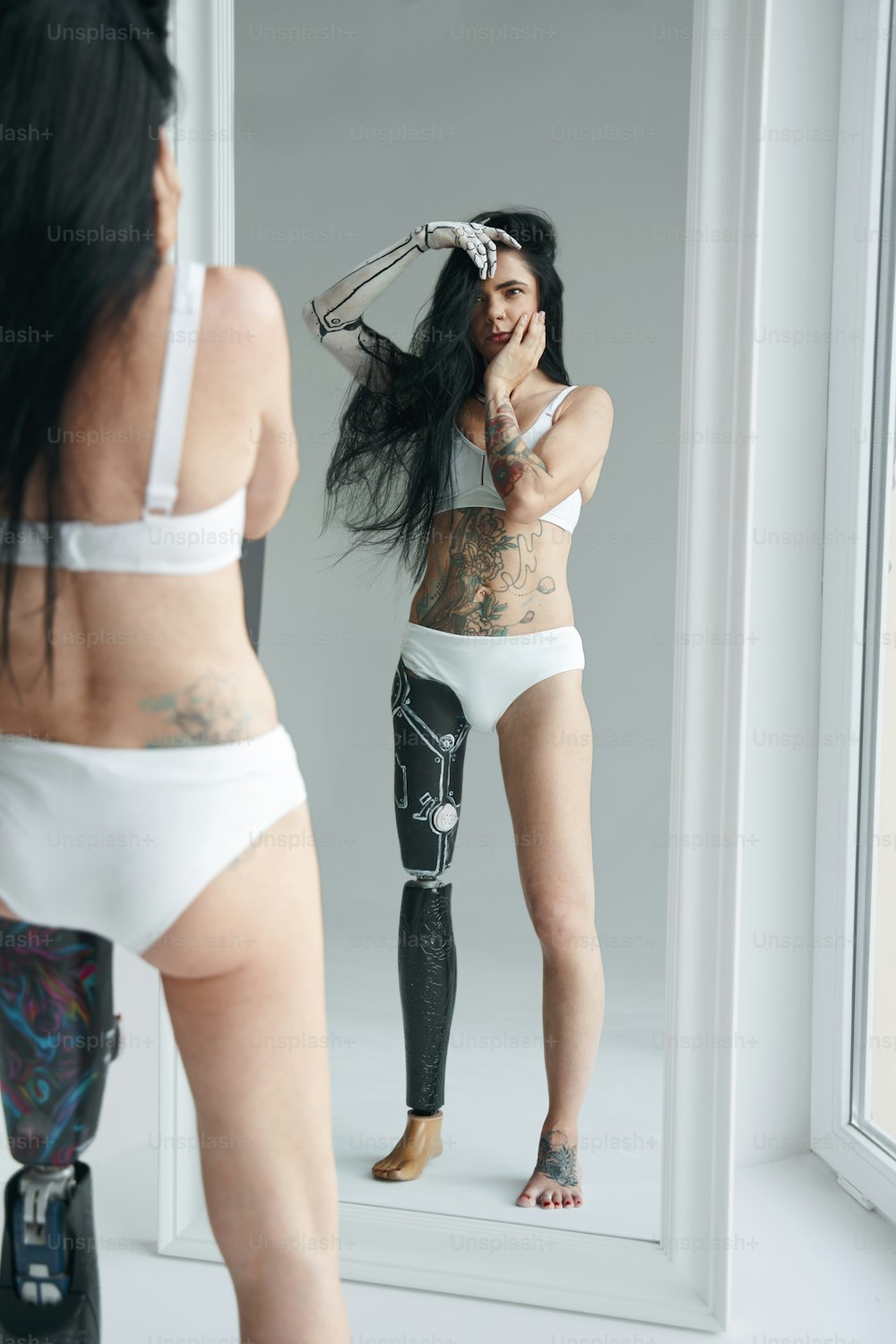 Brunette woman with unusual appearance and futuristic droid body art. Girl standing in front of the mirror and looking at her reflection. Studio photography