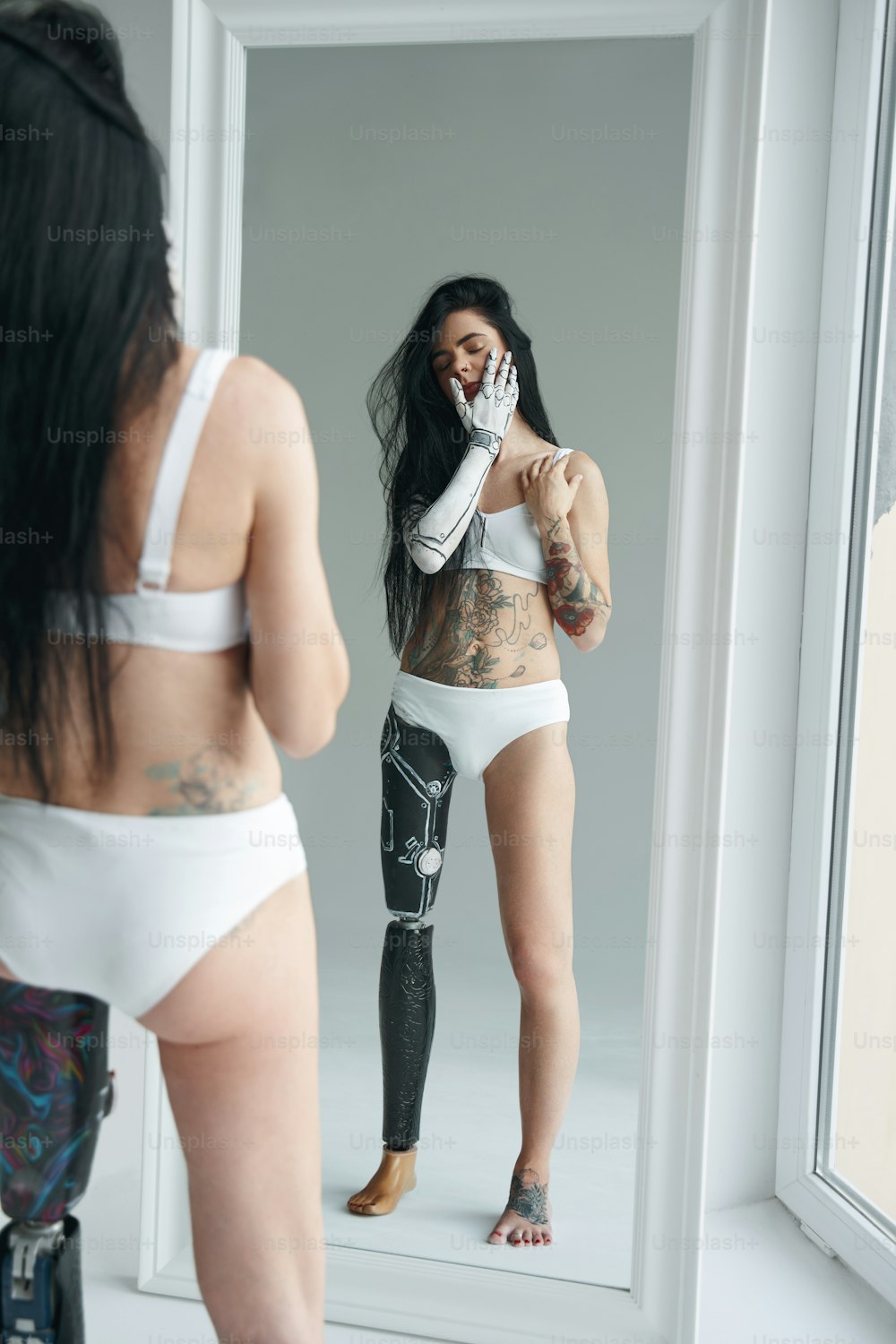 Vista vertical de la mujer tatuada con pata de prótesis y patrón cyborg en su cuerpo mirando su reflejo en el espejo. Concepto de personas con necesidades especiales