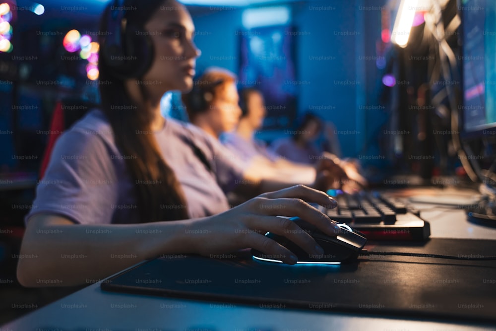Personas sentadas en la sala de estudio profesional de jugadores cibernéticos con sillones de computadora personal, teclado para transmitir en fondo de desenfoque de color neón. Enfoque en la mano femenina