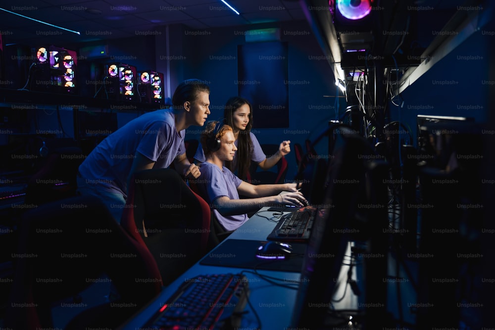 Junges, konzentriertes Team von Profi-Gamern, die aufgeregt sind, während sie gemeinsam im Internetcafé in Online-Cybersportspielen spielen