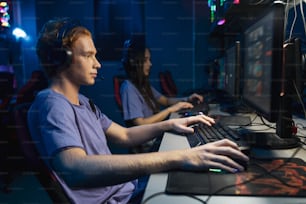 Équipe diversifiée de joueurs professionnels du cybersport portant des écouteurs participant à un tournoi mondial d’eSport, jouant à des jeux vidéo en ligne, vue latérale