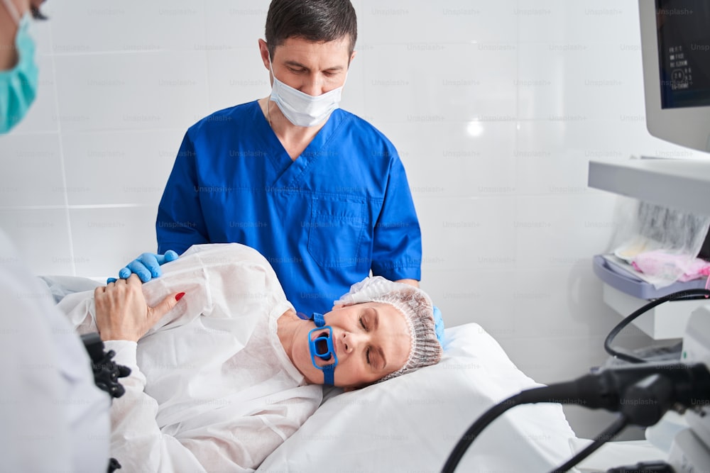 Arzt und Patientin während der Endoskopie im Krankenhaus. Frau, die das Endoskop vor der Gastroskopie am Mund hält. Ärztliches Untersuchungskonzept