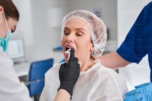 클리닉에서 내시경 검사를 받기 전에 여성 환자의 입에 마취를 뿌리는 세심한 간호사. 내시경 준비 개념