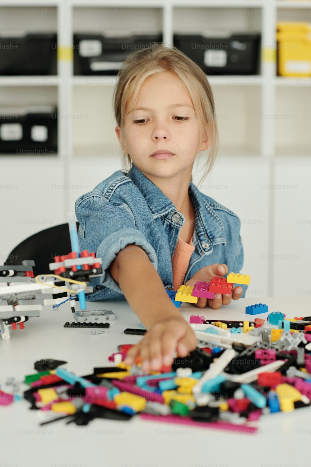 Studentessa carina che prende i dettagli del costruttore mentre è seduta alla scrivania in classe e crea un nuovo modello di robot a lezione