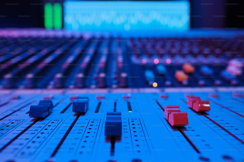 Foto em close-up de botões e controles deslizantes do console de mixagem em luz neon azul no estúdio de gravação moderno