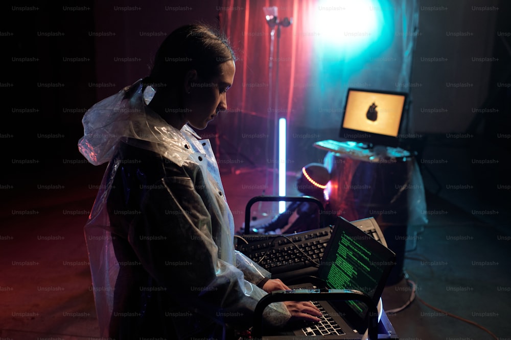 Giovane donna in impermeabile che digita sul computer portatile, sviluppa un nuovo programma e lavora con gli script sullo schermo