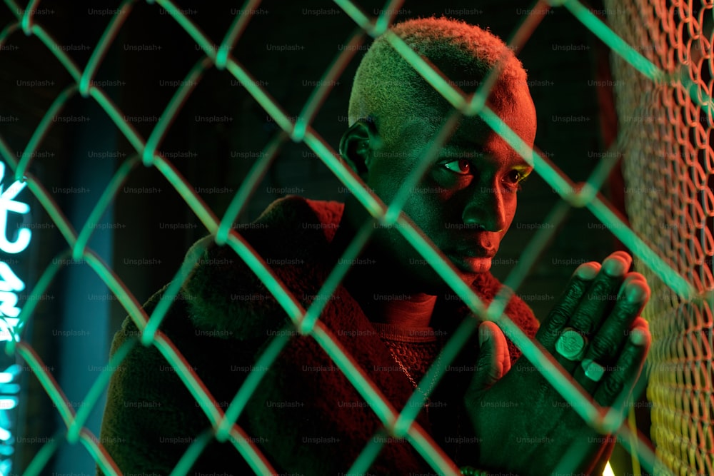 Afrikanischer Cyberpunk-Mann, der seine Hände zusammenlegt und hinter Gittern in der Dunkelheit betet