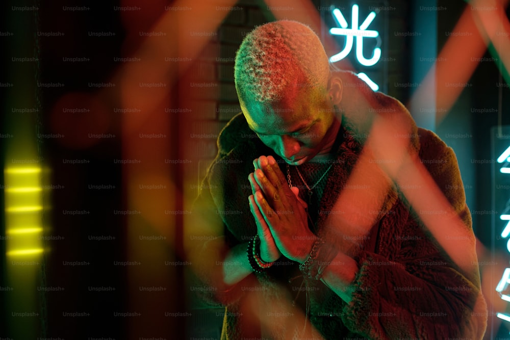 Afrikanischer Cyberpunk-Mann im Pelzmantel, der in der Dunkelheit betet, mit Neon-Hieroglyphen, die Nirvana und westliches Paradies im Hintergrund bedeuten
