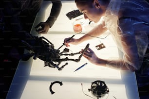Hochwinkelansicht der Frau, die den Cyberpunk-Arm konstruiert, der mit dem menschlichen Körper am Tisch verbunden ist